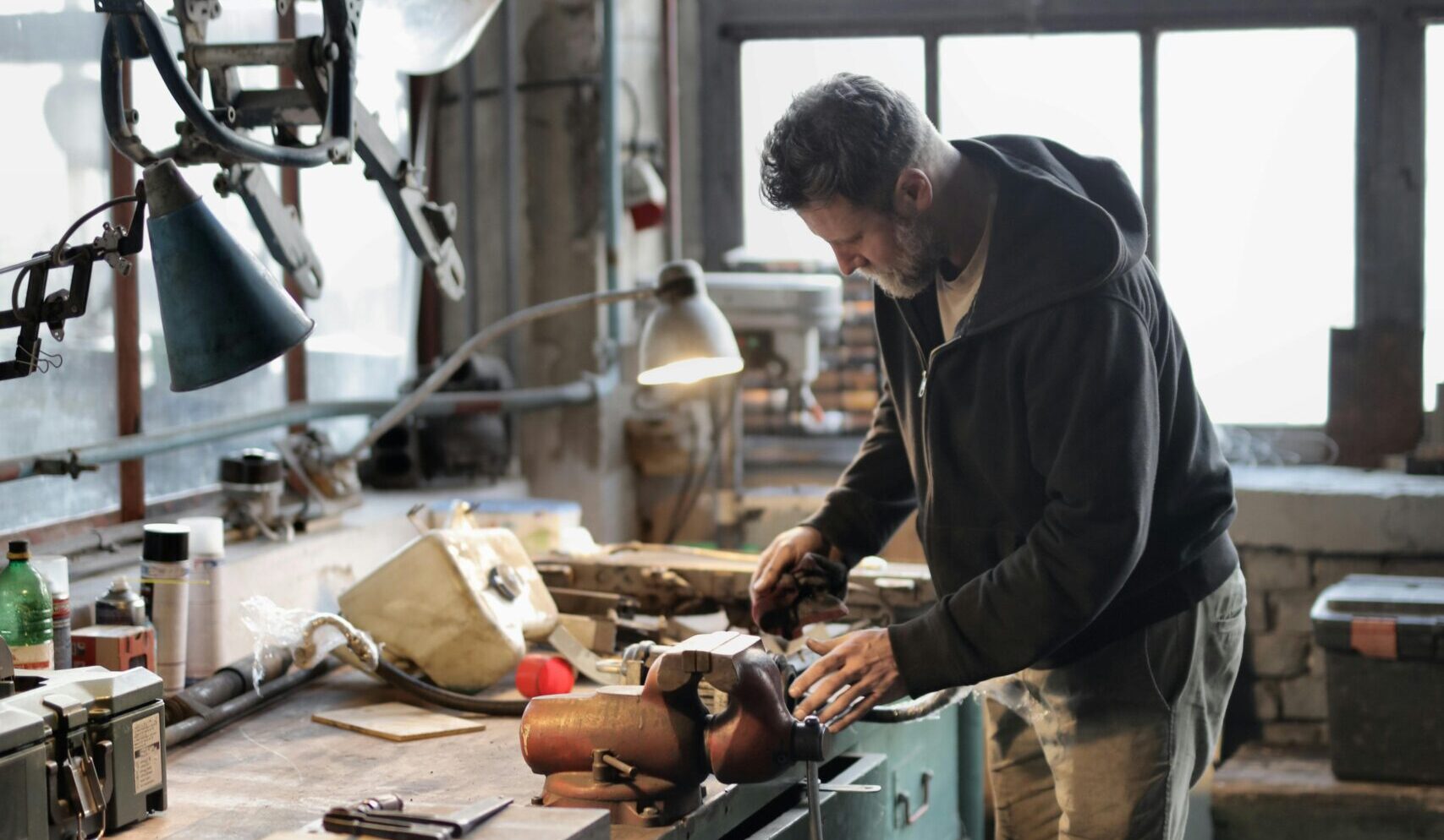 Side view of bearded male master in casual clothes standing at workbench and fixing details with professional metal instrument